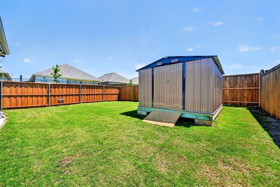 Expansive backyard featuring a lush green lawn, full privacy fencing, and a metal storage shed