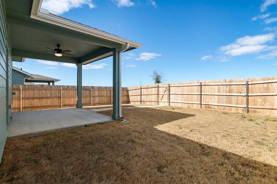 Fenced backyard with ceiling fan and a patio area