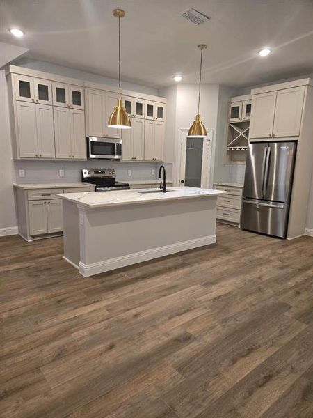 Kitchen featuring pendant lighting, sink, appliances with stainless steel finishes, and an island with sink