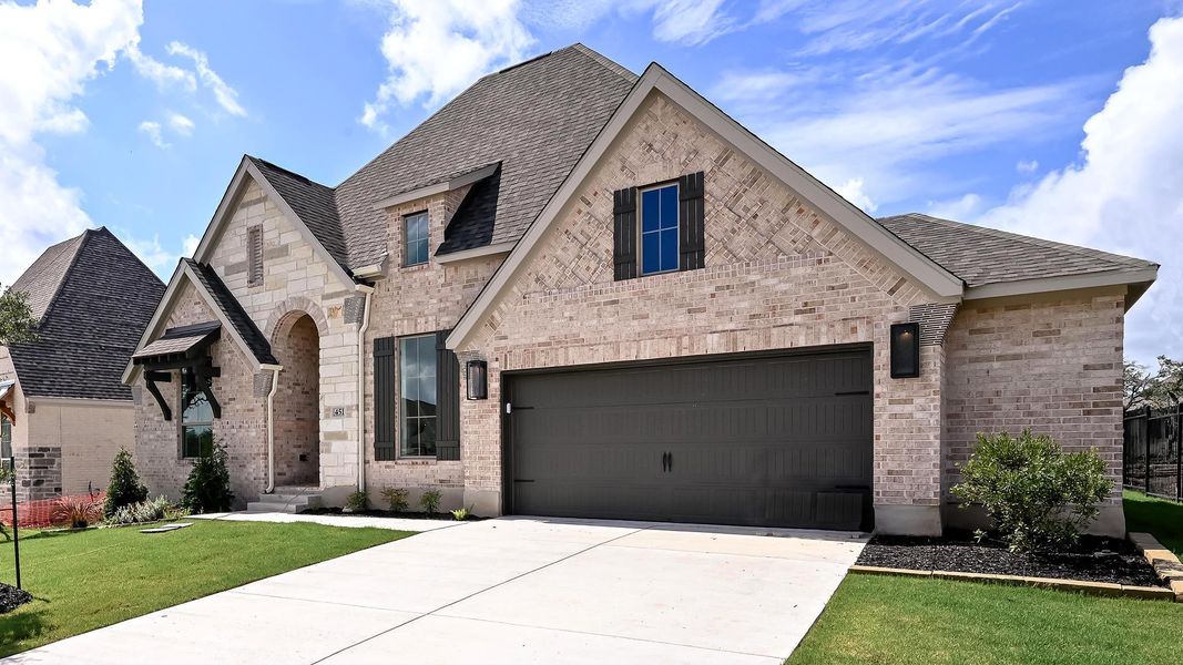 French country home featuring brick siding, concrete driveway, a front lawn, and a shingled roof French country home featuring brick siding, concrete driveway, a front lawn, and a shingled roof