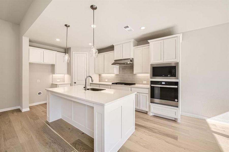 Kitchen with a kitchen island with sink, extractor fan, light hardwood / wood-style flooring, stainless steel appliances, and sink