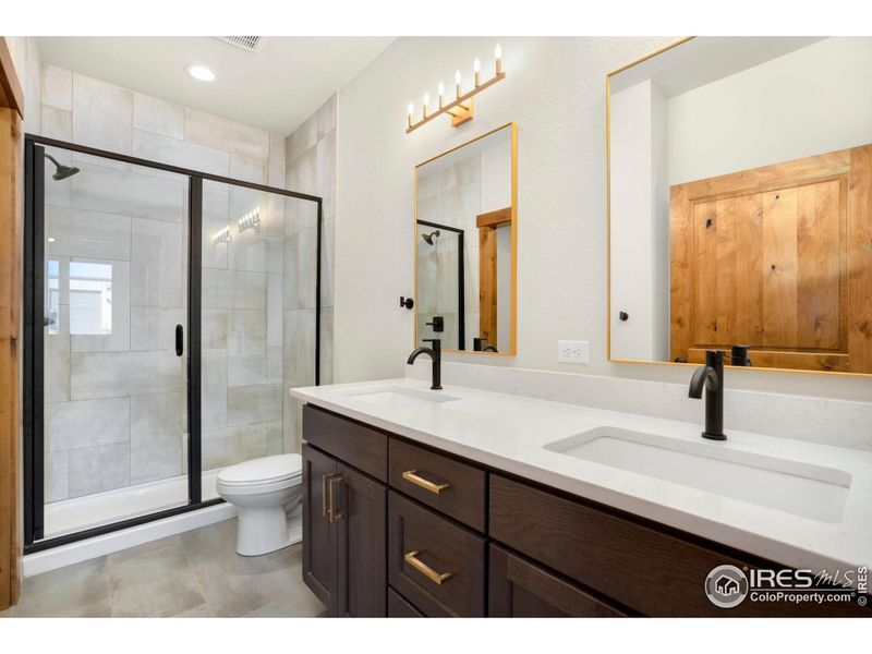 Primary main level bathroom with double sinks, tile, quartz and glass shower door.