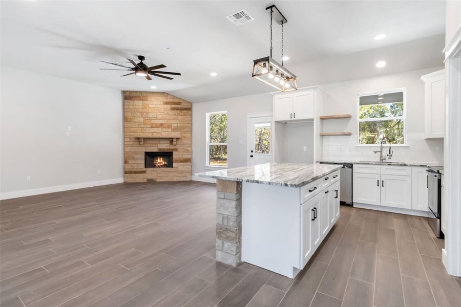 Kitchen featuring a stone fireplace, a center island, white cabinets, and decorative light fixtures