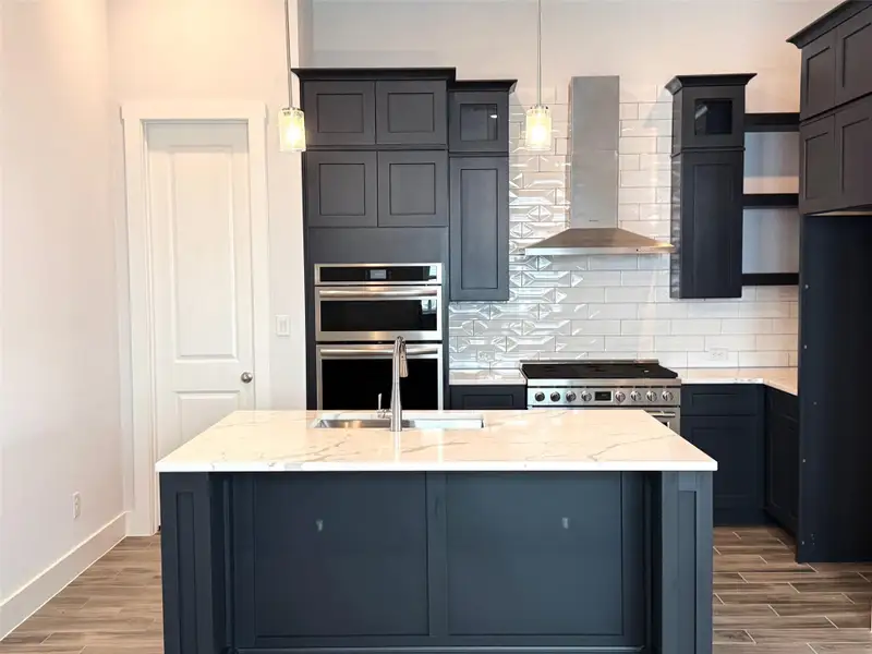 A contemporary kitchen showcasing dark cabinetry, a spacious island with a sink, and sleek stainless steel appliances.