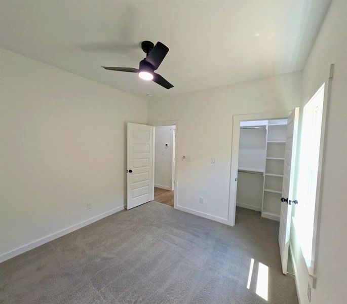 Unfurnished bedroom with a walk in closet, carpet flooring, and a ceiling fan Unfurnished bedroom with a walk in closet, carpet flooring, and a ceiling fan