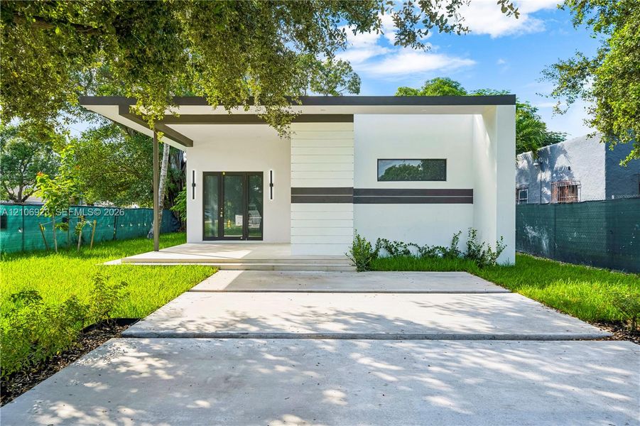 Modern exterior featuring smooth white stucco finish, flat roofline with dark trim, expansive concrete driveway, covered porch, and vertical wall-mounted lighting fixtures Modern exterior featuring smooth white stucco finish, flat roofline with dark trim, expansive concrete driveway, covered porch, and vertical wall-mounted lighting fixtures