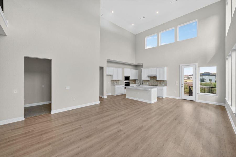 Unfurnished living room with light wood finished floors, a high ceiling, and recessed lighting Unfurnished living room with light wood finished floors, a high ceiling, and recessed lighting