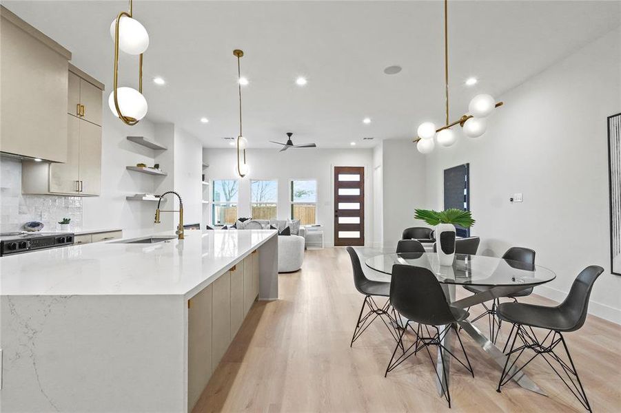 Kitchen featuring open shelves, hanging light fixtures, an island with sink, and light wood-style floors