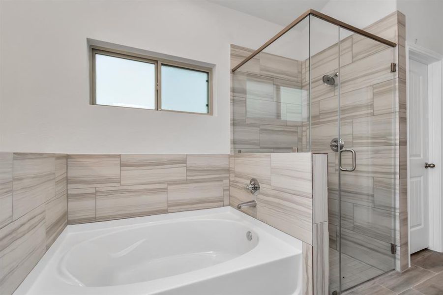 Indulge in the spa-like experience of this primary bathroom, featuring a soaking tub and a glass-enclosed shower. The elegant tile work and modern fixtures create a tranquil retreat where you can unwind after a long day. Natural light pours in through the frosted window, enhancing the serene atmosphere of this luxurious space. **This image is from another Saratoga Home - Wren floorplan.**