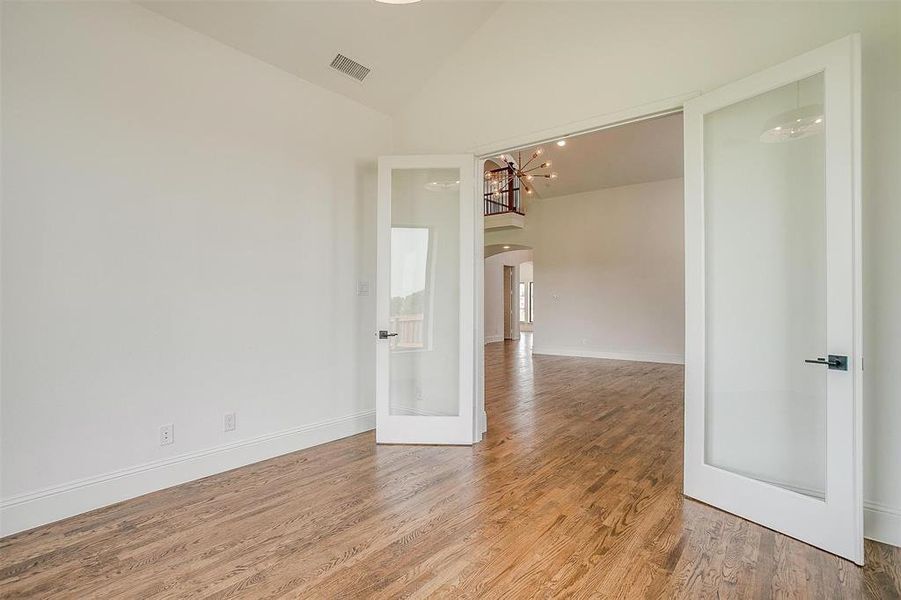 Empty room featuring high vaulted ceiling, a chandelier, and wood-type flooring