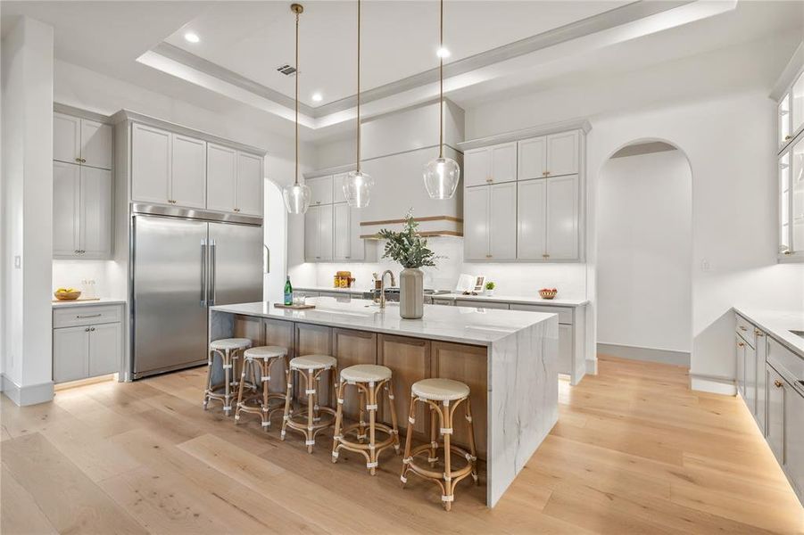 Kitchen featuring built in fridge, a tray ceiling, light wood-style flooring, arched walkways, and a kitchen bar Kitchen featuring built in fridge, a tray ceiling, light wood-style flooring, arched walkways, and a kitchen bar
