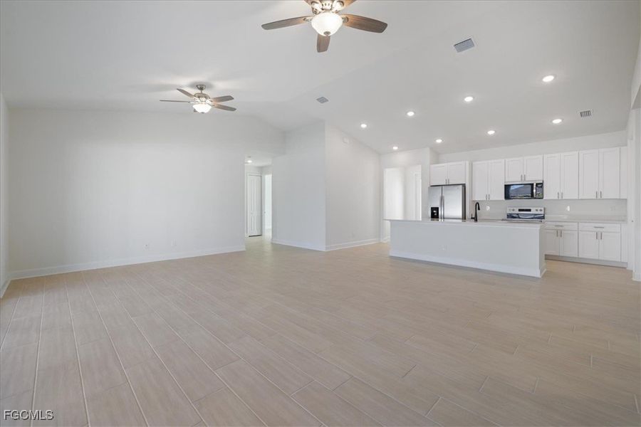 Unfurnished living room featuring wood tiled floors, ceiling fan, recessed lighting, and vaulted ceiling Unfurnished living room featuring wood tiled floors, ceiling fan, recessed lighting, and vaulted ceiling