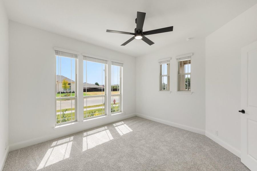 Empty bedroom with carpet flooring, black ceiling fan, and large windows with neighborhood views