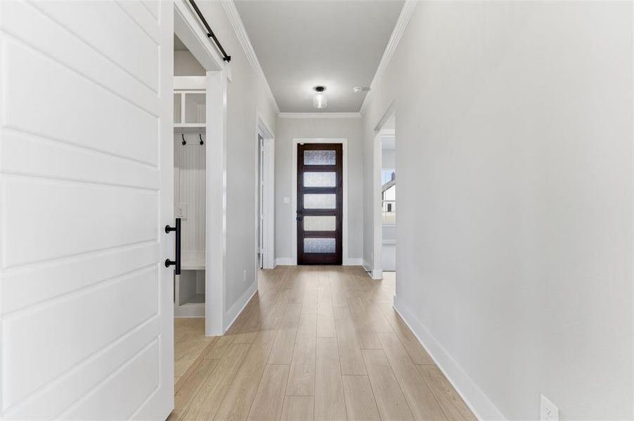Entryway with a barn door, ornamental molding, and wood finished floors