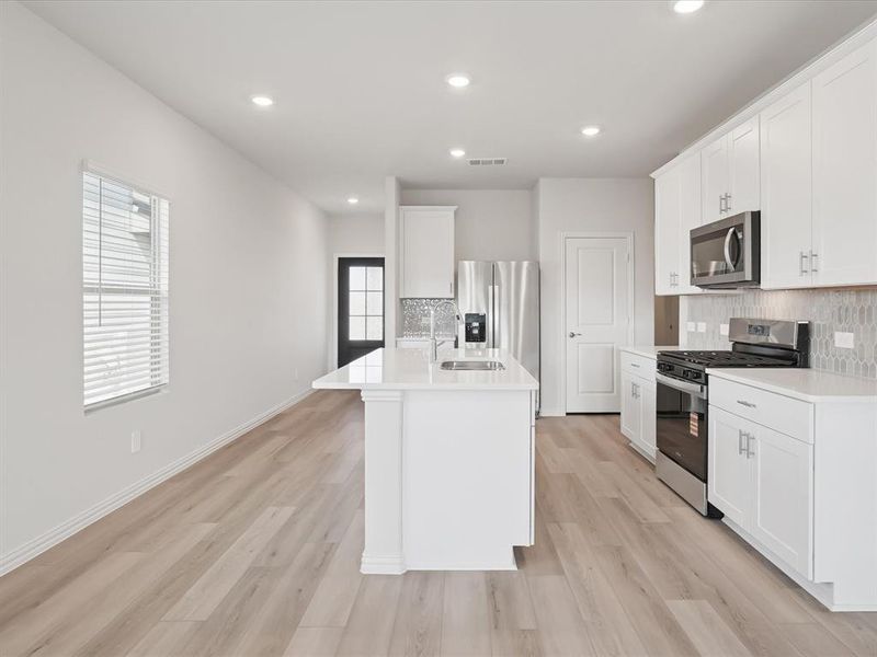 Kitchen featuring stainless steel appliances, backsplash, an island with sink, white cabinets, and recessed lighting