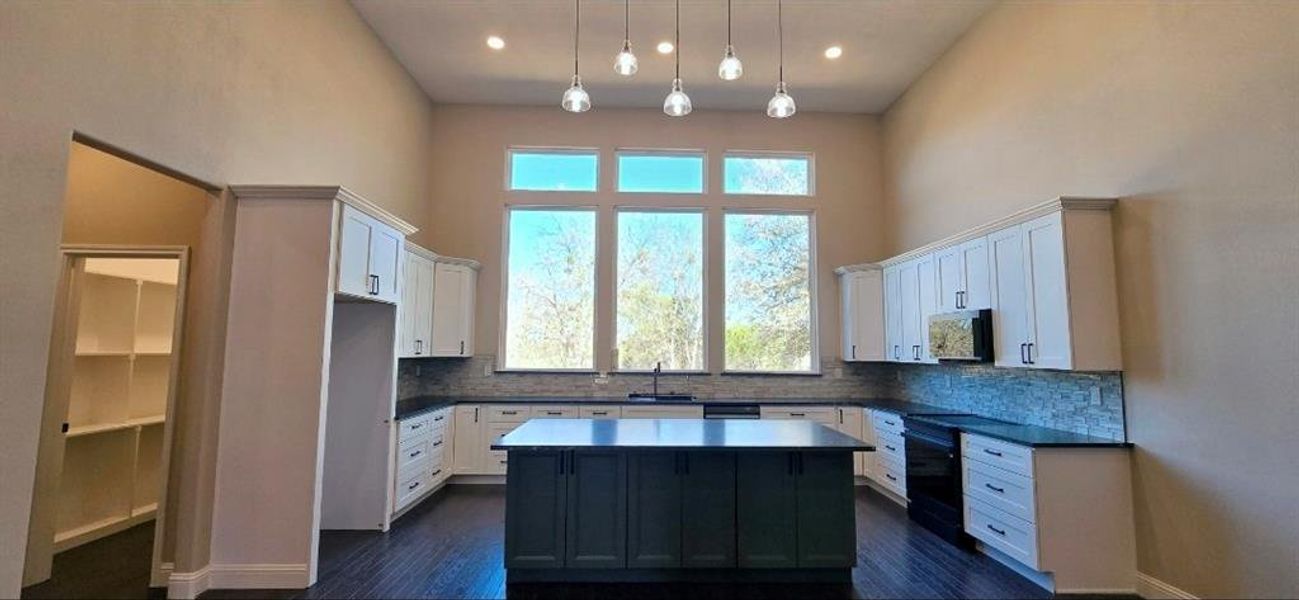 Kitchen with white cabinetry, a high ceiling, hanging light fixtures, a large center island, and dark wood-type flooring Kitchen with white cabinetry, a high ceiling, hanging light fixtures, a large center island, and dark wood-type flooring