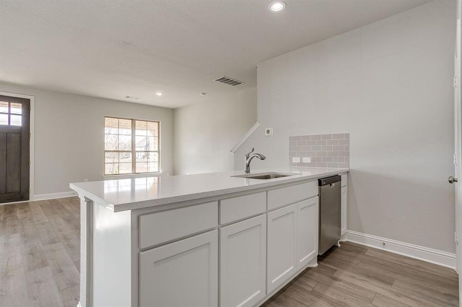 Kitchen with a peninsula, white cabinetry, light wood finished floors, dishwasher, and recessed lighting