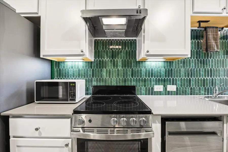 Kitchen featuring stainless steel appliances, extractor fan, white cabinetry, and backsplash Kitchen featuring stainless steel appliances, extractor fan, white cabinetry, and backsplash