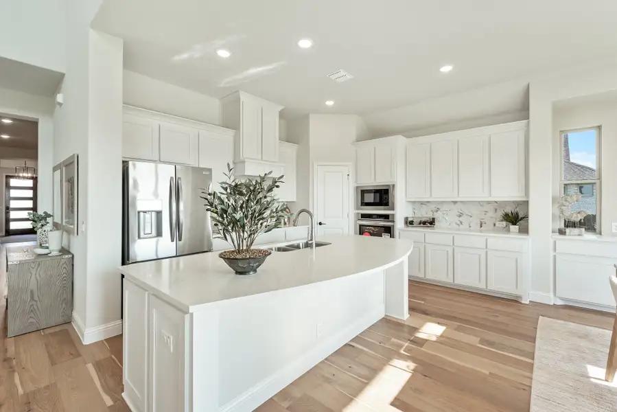 White kitchen with large center island, stainless steel appliances, and light hardwood floors