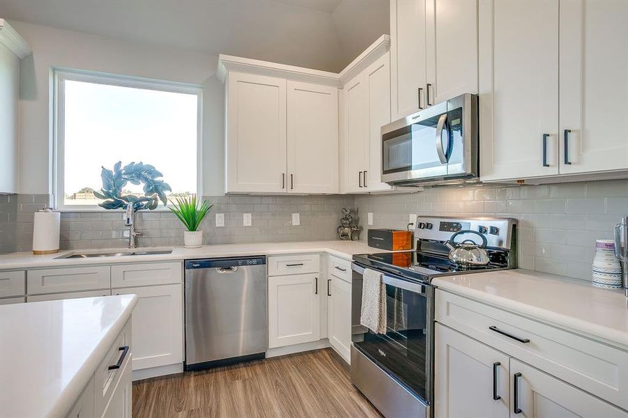Kitchen with stainless steel appliances, white cabinetry, light wood-style flooring, and tasteful backsplash