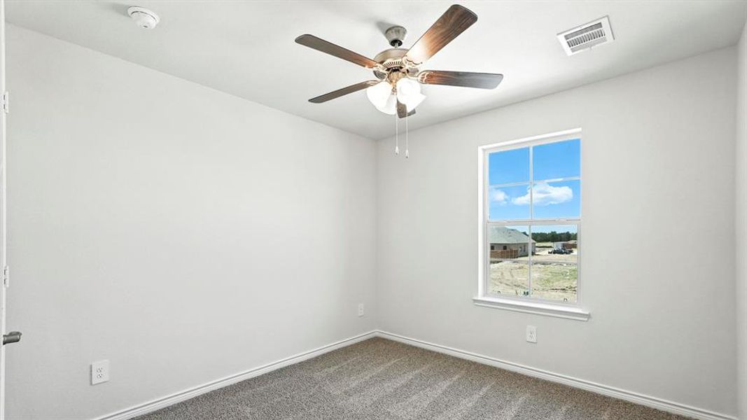 Carpeted interior room featuring a ceiling fan with light fixture, window with grid panes, white trim, and a white smoke detector