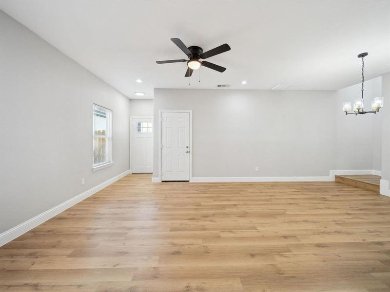 Empty room with ceiling fan with notable chandelier and light wood-type flooring