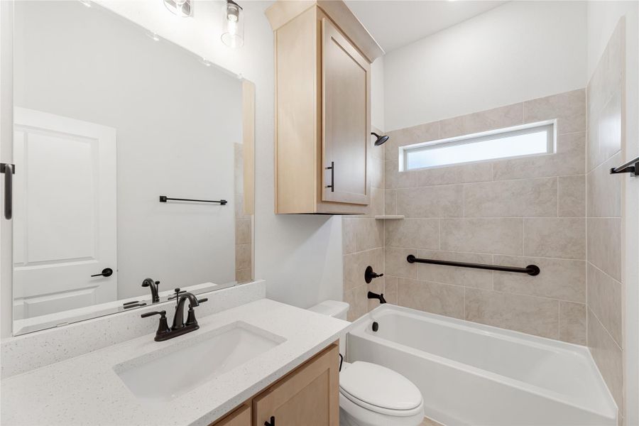 Bathroom with quartz countertop vanity, tiled tub-shower combo, and light wood cabinet above toilet