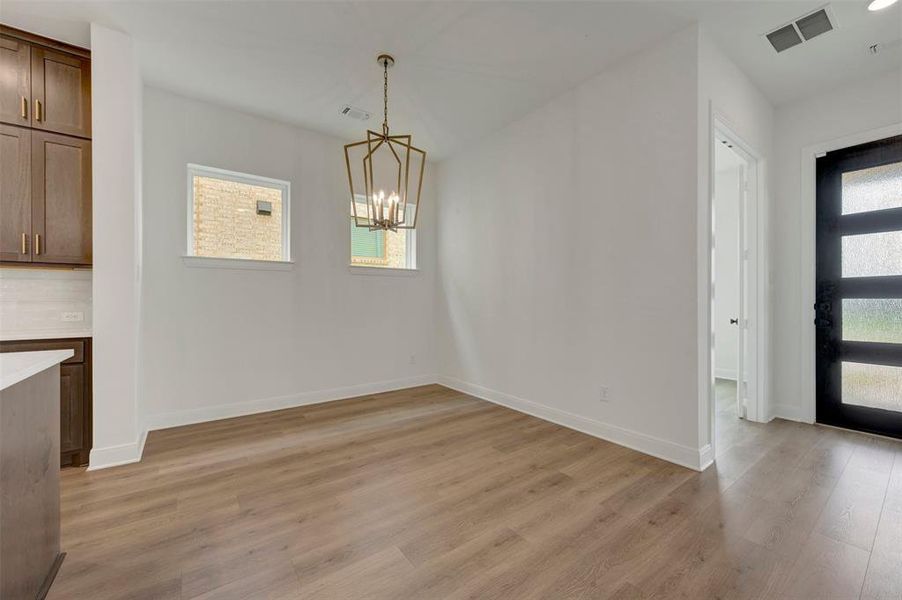 Open-concept living area featuring wood-finish flooring, a contemporary chandelier, two windows providing natural light, and a modern entry door with frosted glass panels