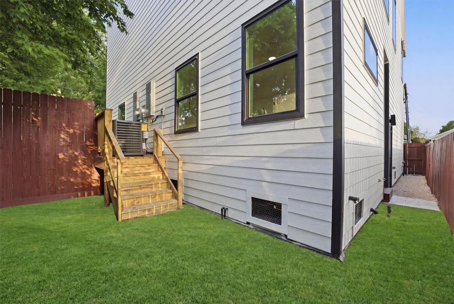 Private, low-maintenance side yard featuring artificial turf, privacy fencing, modern exterior siding, and wood stairs leading to an elevated deck, offering functional outdoor space with easy access to the home.