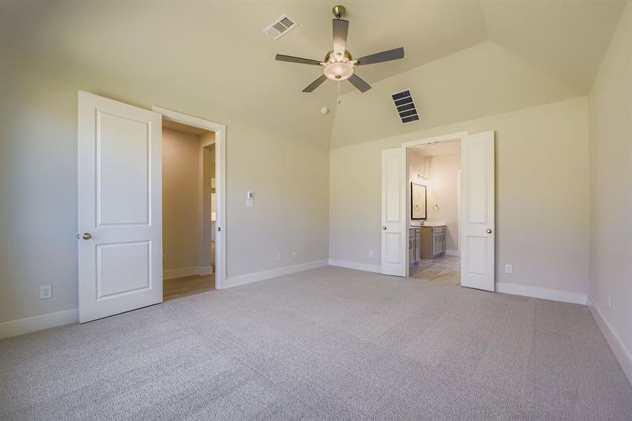 Unfurnished bedroom with light colored carpet, ensuite bathroom, a ceiling fan, and vaulted ceiling