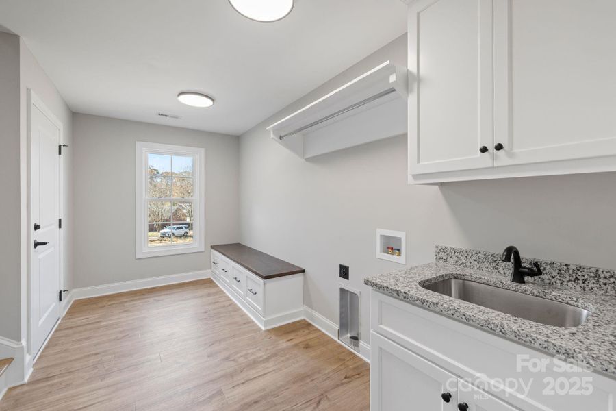 Spacious laundry and mudroom combo featuring built-in bench w/ storage, hanging rack, and a granite-topped utility sink—offering both function and convenience. Spacious laundry and mudroom combo featuring built-in bench w/ storage, hanging rack, and a granite-topped utility sink—offering both function and convenience.
