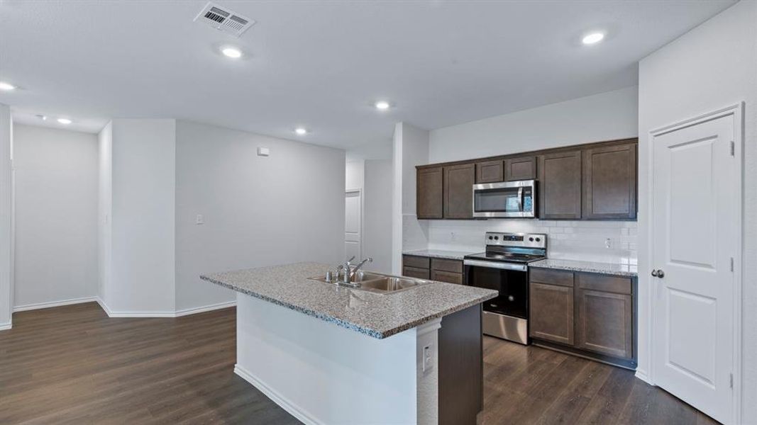 Kitchen with stainless steel appliances, dark wood finish cabinetry, dark wood-style flooring, an island with sink, and recessed lighting
