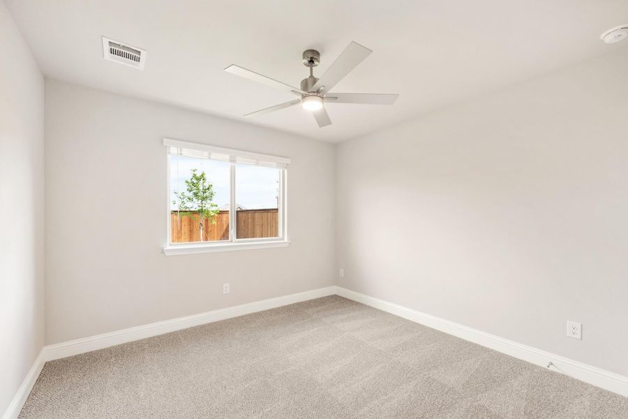 Empty bedroom with gray carpet, ceiling fan, and single window with backyard view