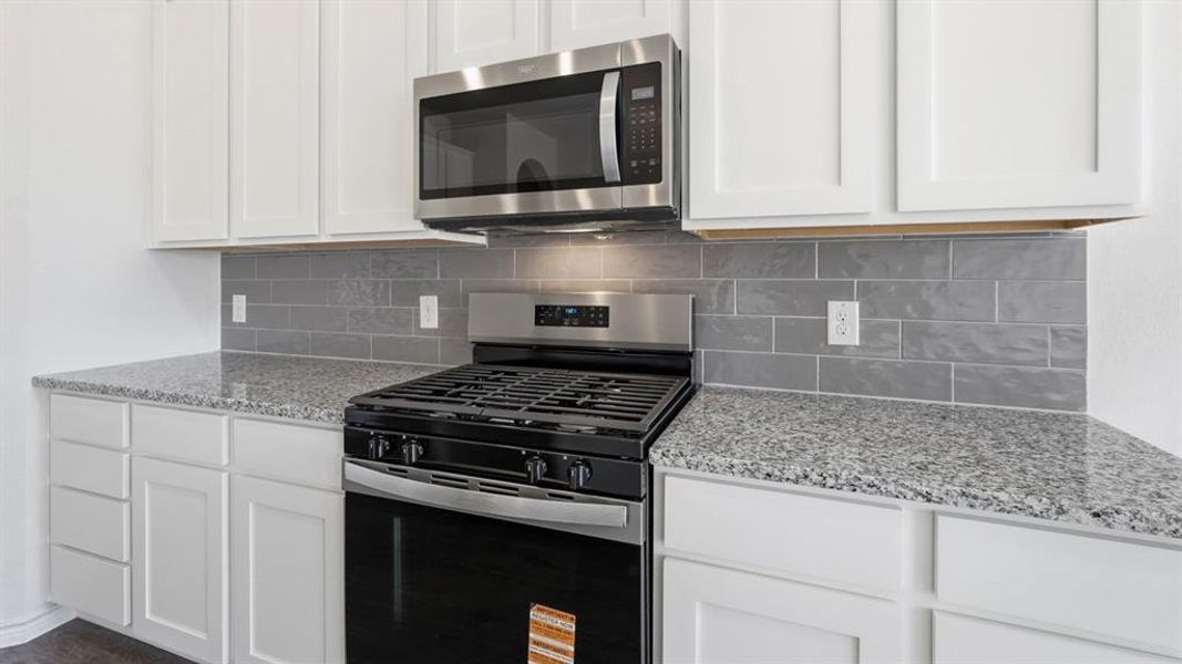 Kitchen with appliances with stainless steel finishes, light stone countertops, white cabinetry, and tasteful backsplash Kitchen with appliances with stainless steel finishes, light stone countertops, white cabinetry, and tasteful backsplash