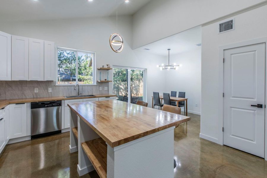 Kitchen featuring concrete flooring, decorative backsplash, butcher block countertops, hanging light fixtures, and white cabinets