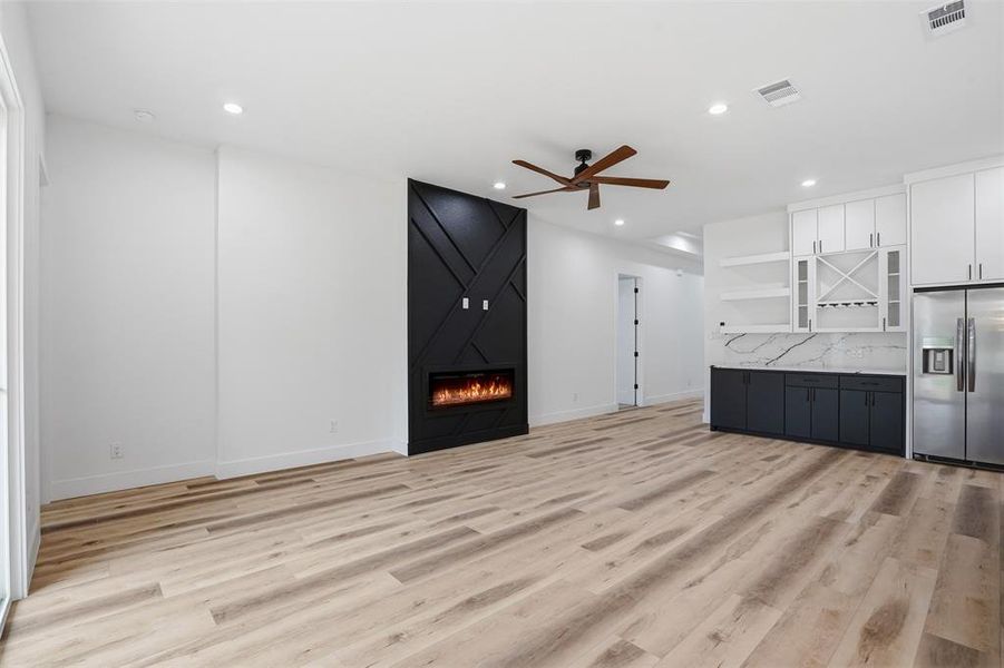Spacious living area featuring light wood-finish flooring, a modern black accent wall with an electric fireplace, recessed lighting, and a ceiling fan