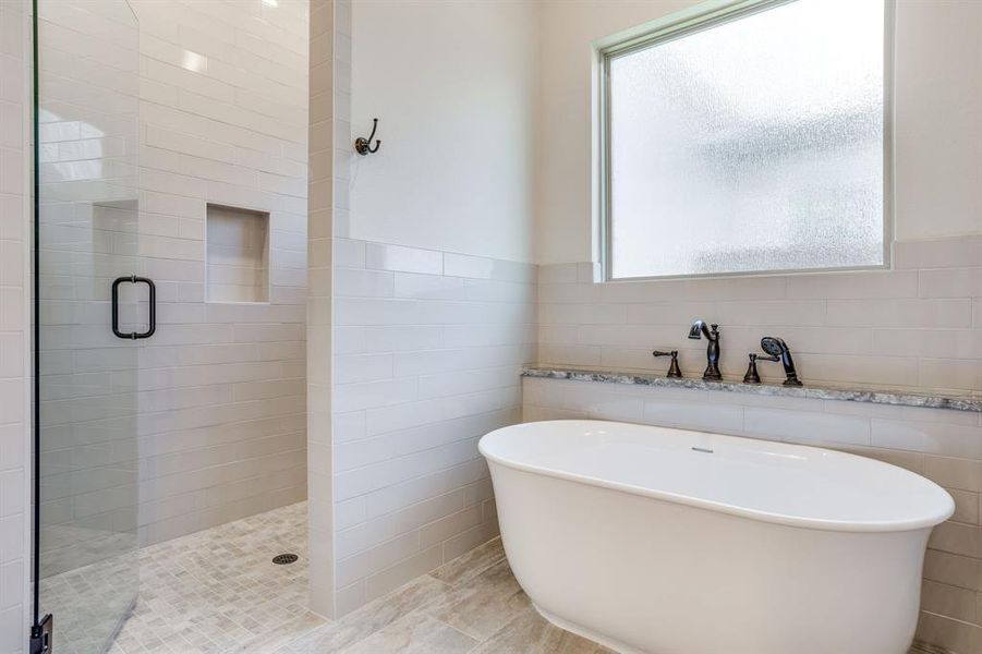 Contemporary bathroom featuring a freestanding soaking tub, a separate glass-enclosed shower with subway tile surround, a built-in shower niche, and a privacy window