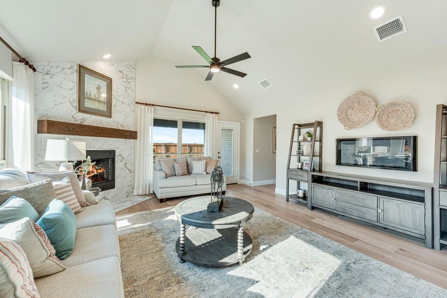 Living room with vaulted ceiling, marble fireplace, hardwood floors, and ceiling fan