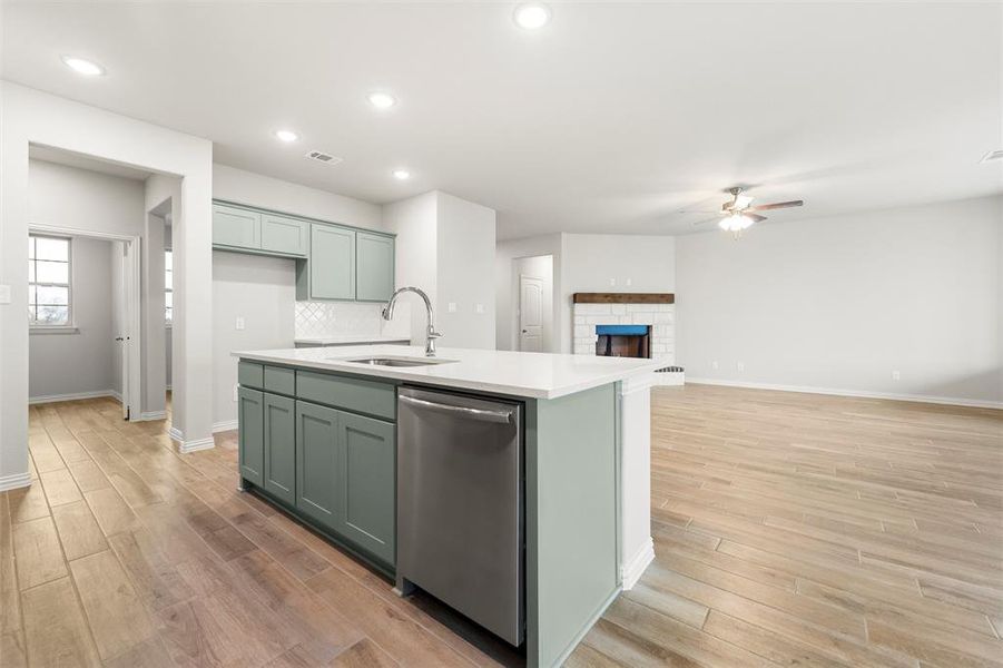 Kitchen featuring green cabinetry, dishwasher, a kitchen island with sink, light wood finished floors, and open floor plan Kitchen featuring green cabinetry, dishwasher, a kitchen island with sink, light wood finished floors, and open floor plan