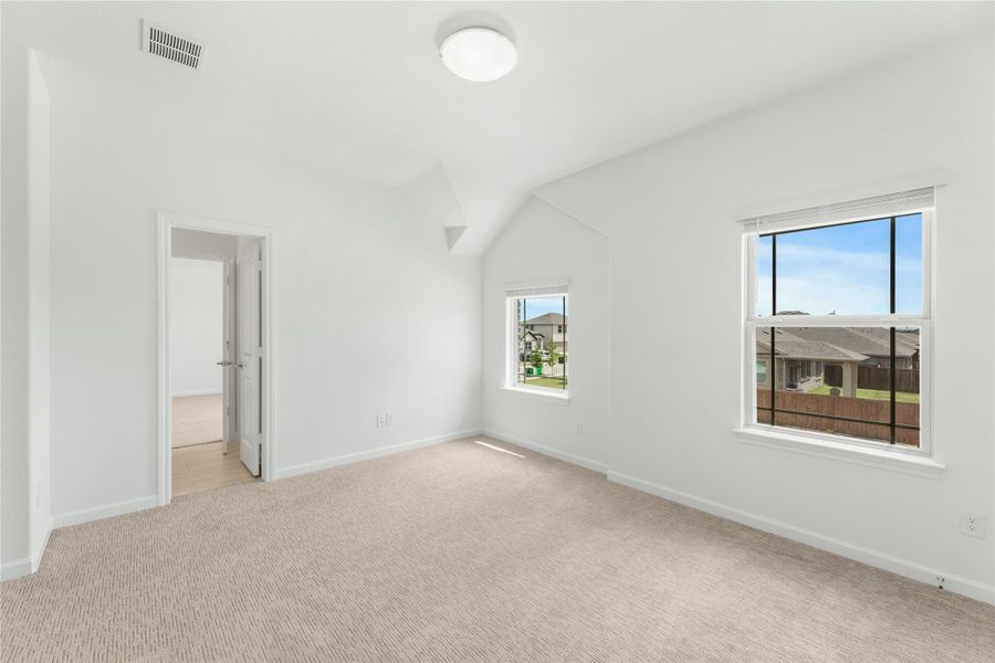 Empty bedroom with vaulted ceiling, beige carpet, white walls, and two windows with neighborhood views