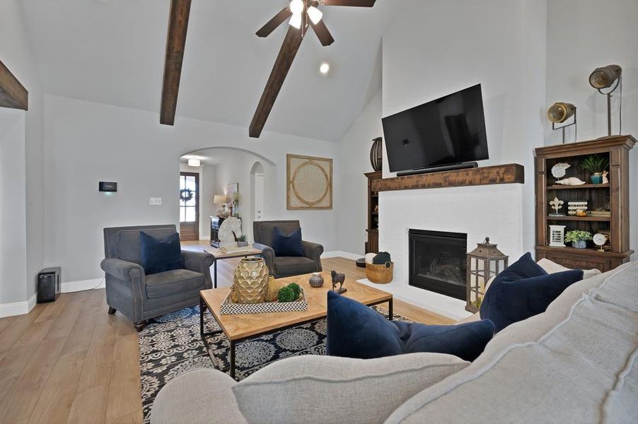 Living room with high vaulted ceiling, arched walkways, wood finished floors, a brick fireplace, and a ceiling fan Living room with high vaulted ceiling, arched walkways, wood finished floors, a brick fireplace, and a ceiling fan