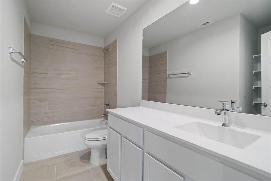 Secondary bath features tile flooring, bath/shower combo with tile surround, stained wood cabinets, beautiful light countertops, mirror, sleek fixtures and modern finishes!