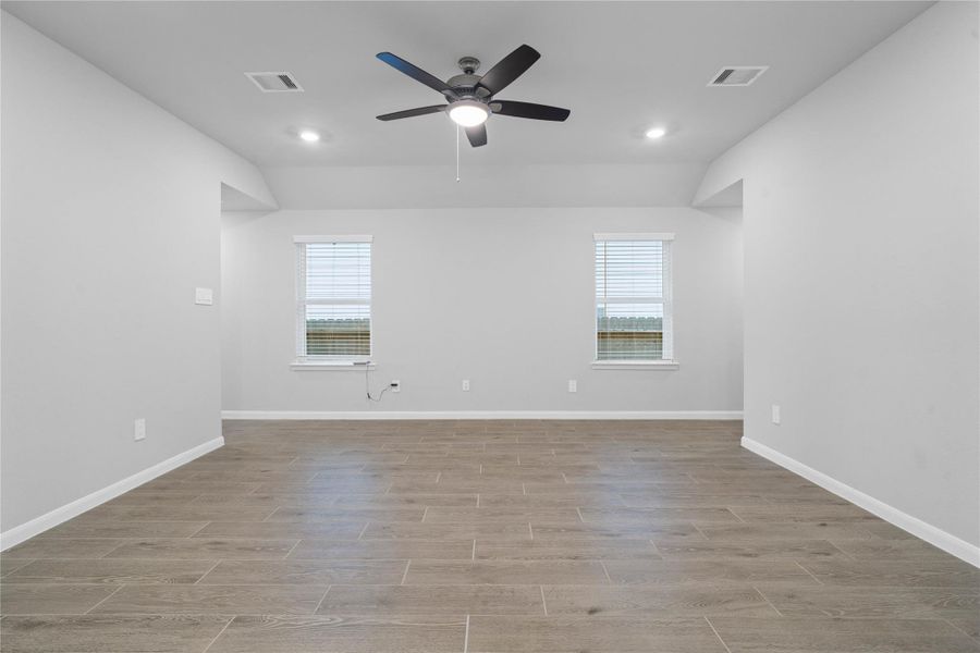 A bright and airy open-concept space featuring tile flooring, sloped ceilings with recessed lighting and ceiling fan, abundant natural light from large windows (fitted with blinds), and an access door to the back covered patio located to the right.