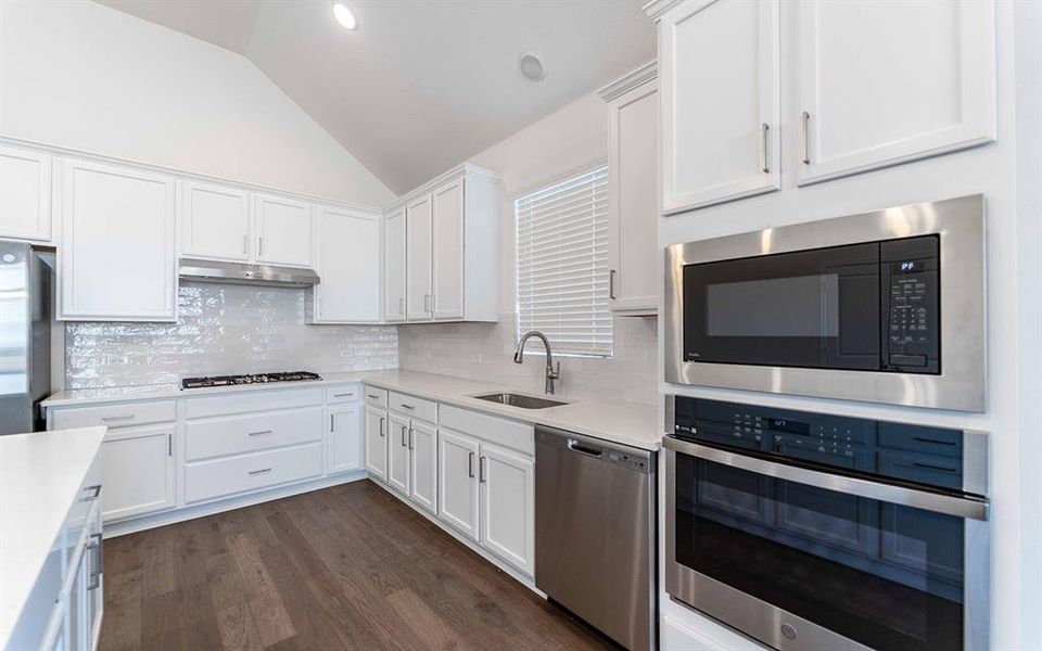 Bright kitchen featuring white cabinetry, light countertops, stainless steel appliances, wood-finish flooring, and a vaulted ceiling