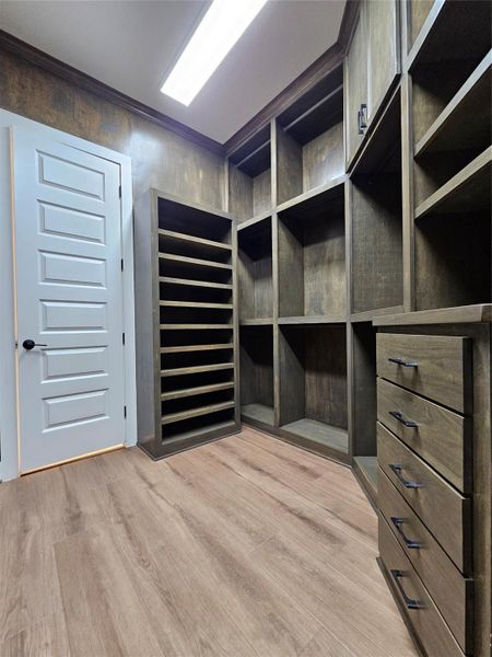 This photo shows a spacious walk-in closet with custom wood shelving and drawers, ample storage space, and a modern design. The room is well-lit, featuring a light wood floor and a sleek white door. This photo shows a spacious walk-in closet with custom wood shelving and drawers, ample storage space, and a modern design. The room is well-lit, featuring a light wood floor and a sleek white door.
