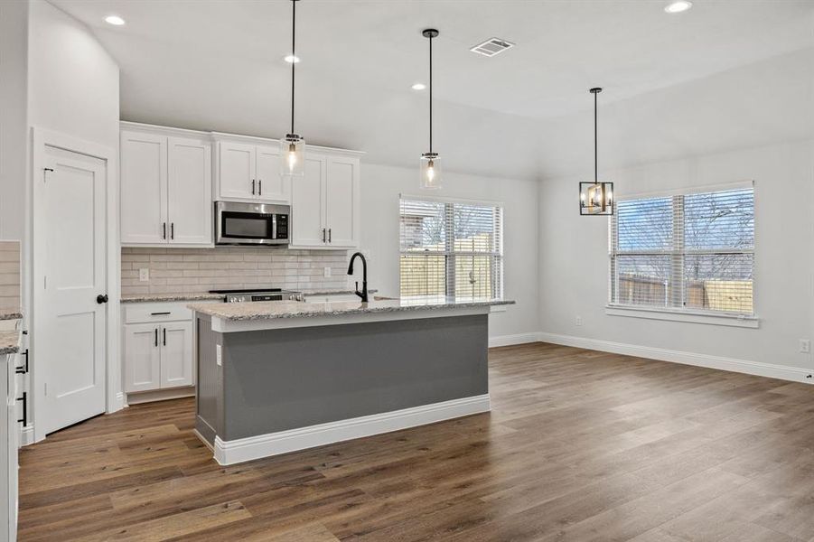 Kitchen featuring light stone countertops, a center island with sink, hanging light fixtures, white cabinets, and recessed lighting