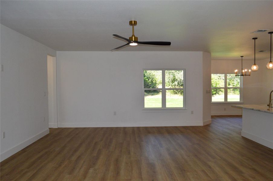 Unfurnished living room with dark wood-type flooring, a ceiling fan, and a chandelier Unfurnished living room with dark wood-type flooring, a ceiling fan, and a chandelier