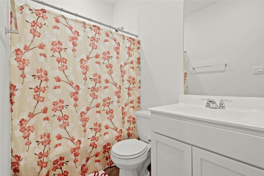 A clean and simple guest bath, conveniently located off the main foyer and featuring a crisp white vanity and modern wood-style flooring.