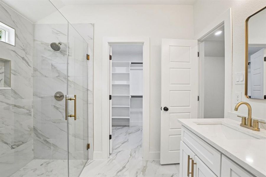 Bathroom with a marble finish shower, vanity, a walk in closet, and light marble finish floors Bathroom with a marble finish shower, vanity, a walk in closet, and light marble finish floors