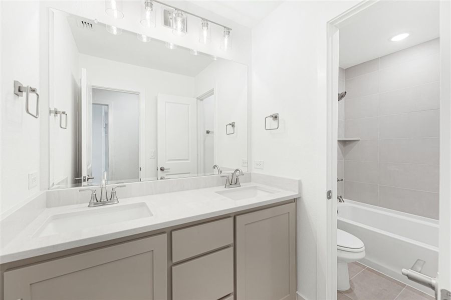 Bathroom with double sink vanity, gray cabinets, white countertop, and tiled shower-tub combo